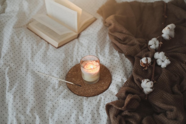 Acogedores detalles interiores de bodegones con una vela de libro y una ramita de algodón en una cama cálida y suave dulce hogar