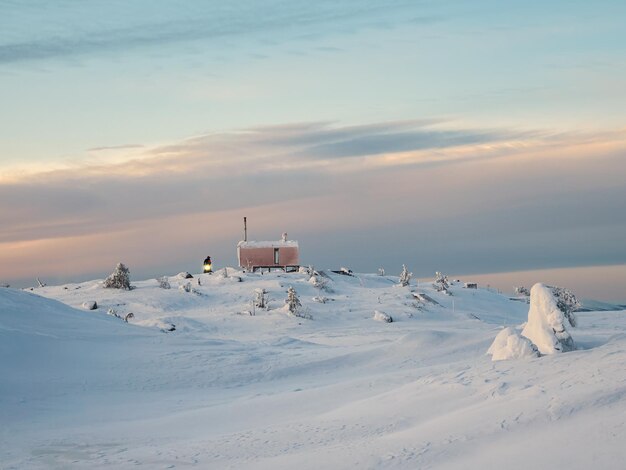 Aconchegante casa de hóspedes do norte em uma colina nevada ao amanhecer Cabine no amanhecer de inverno Casa solitária no topo de uma colina na manhã fria Dubldom na montanha Volodyanaya Kandalaksha região de Murmansk na Rússia