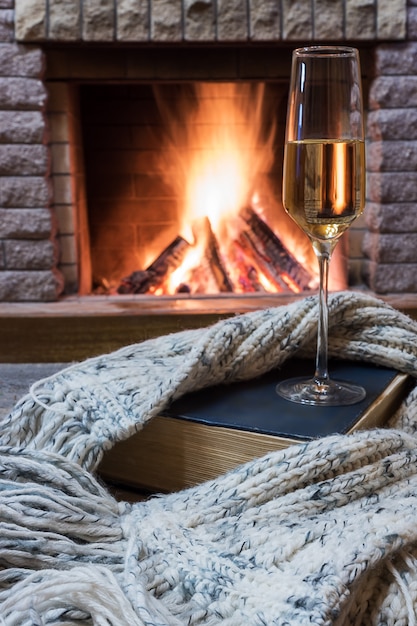 Aconchegante cena antes da lareira com um copo de vinho, livro e lã cachecol quente.