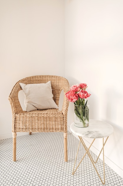 Aconchegante e confortável espaço de descanso em casa com cadeira de vime, parede branca, ladrilho de mosaico, mesa de mármore com um lindo buquê de flores de peônia.