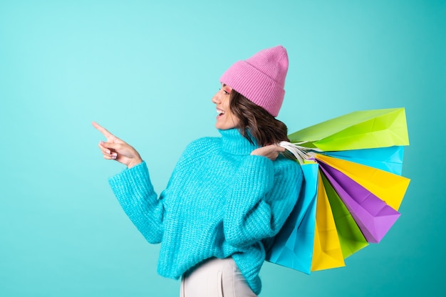 Aconchegante retrato de uma jovem com um suéter azul de tricô e um chapéu rosa com maquiagem brilhante guarda sacolas de compras