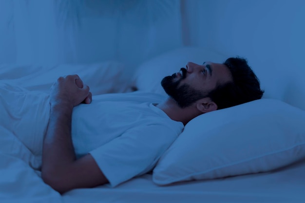 Acordado, sem dormir, chateado, homem indiano, deitado na cama sozinho à noite