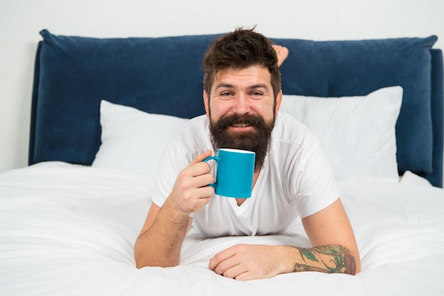 Acorde e sinta o cheiro do café hipster feliz bebe café de manhã homem barbudo gosta de café na cama bebida quente chá de café da manhã humor relaxante bom dia começa com café