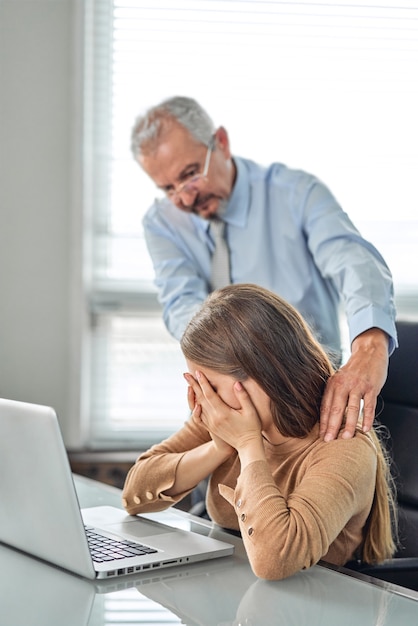 Acoso con un jefe tocando el brazo a su secretaria que está sentada en su lugar de trabajo en la oficina