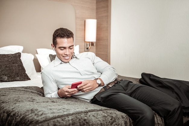 Acostado en la cama. Hombre de negocios acostado en la cama del hotel y relajarse usando el teléfono después de un vuelo largo y agotador