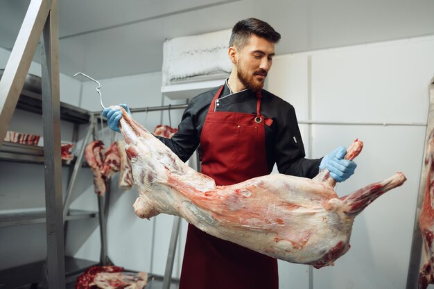 Açougueiro masculino aguardando carne pendurada no gancho na loja de carne