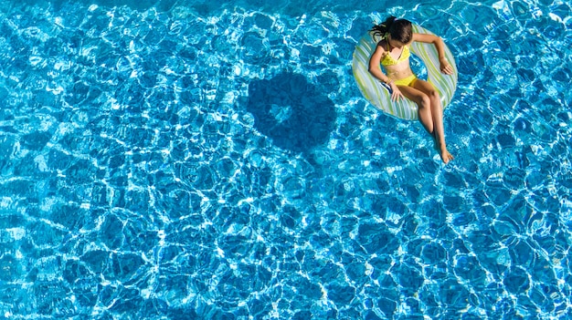 Acrive niña en la piscina vista aérea desde arriba, el niño nada en anillo inflable donut, el niño se divierte en el agua azul en el resort de vacaciones familiares