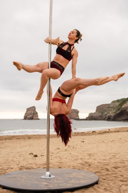 Acrobacias de Pole Dance na areia da praia de Hendaya França Duas jovem caucasiana fazendo pole dance ao nascer do sol em uma bela praia