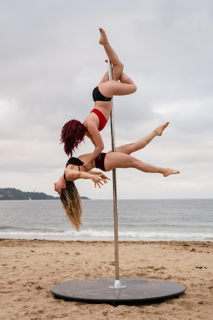 Acrobacias de pole dance viradas para baixo na areia da praia de Hendaya França Duas jovem caucasiana fazendo pole dance ao nascer do sol em uma bela praia