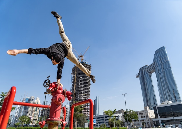 Acrobat flexible mantiene el equilibrio con una mano en la boca de incendios con el paisaje urbano borroso de Dubai. Concepto de modernidad y seguridad.