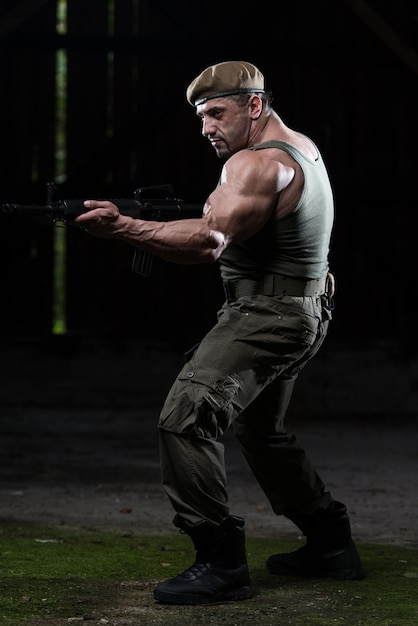 Action-Held bemuskelter Mann mit Maschinengewehr, der in einem verlassenen Gebäude mit grünen Hosen steht