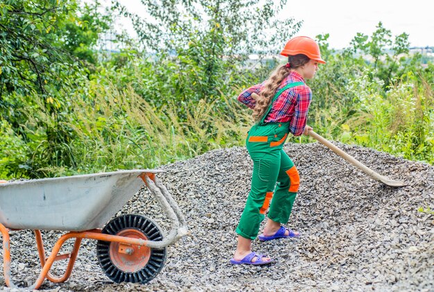 Actividad al aire libre. niña que transporta escombros en una carretilla. trabajo de construcción. constructor de niña toma una pala de escombros. juventud trabajadora. juego de constructor y constructor.