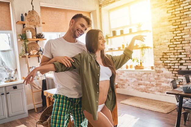 Actividad en casa. Feliz hombre barbudo de pie detrás de su novia mientras se divierten juntos. Concepto doméstico