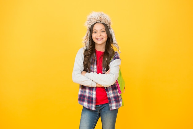 Actividad después de la escuela. De vuelta a la escuela. Mochila de colegiala fondo amarillo. no hay clases esta semana. alumno infantil. eventos de invierno en la escuela. niña pequeña usa sombrero con orejeras. tiempo de escuela de invierno y vacaciones.