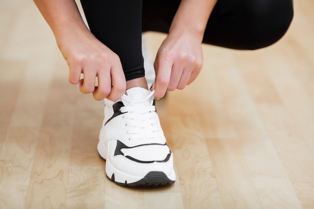 Actividad física, primer plano de niña atar cordones de zapatos deportivos en el gimnasio