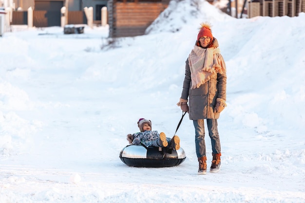 Actividad de invierno de la madre y el niño de la familia juntos en tubos de nieve en la carretera de nieve de invierno