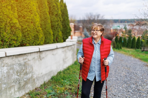 Actividades al aire libre concepto de personas y vacaciones Atractiva mujer de mediana edad de pelo corto en ropa deportiva haciendo senderismo en el bosque usando bastones para caminar nórdico haciendo ejercicio aeróbico disfrutando de la naturaleza