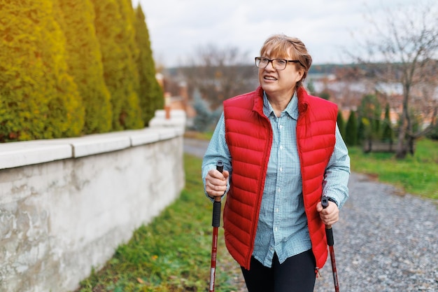 Actividades al aire libre concepto de personas y vacaciones Atractiva mujer de mediana edad de pelo corto en ropa deportiva haciendo senderismo en el bosque usando bastones para caminar nórdico haciendo ejercicio aeróbico disfrutando de la naturaleza