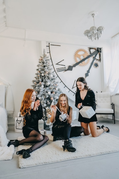 Acto de regalos de navidad dando tres amigas abriendo regalos de navidad juntos en casa joven feliz