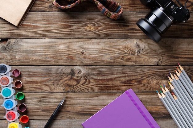 Acuarelas, lápices de colores y cuaderno de bocetos sobre mesa de madera. Foto laica plana con espacio vacío para logotipo, texto.