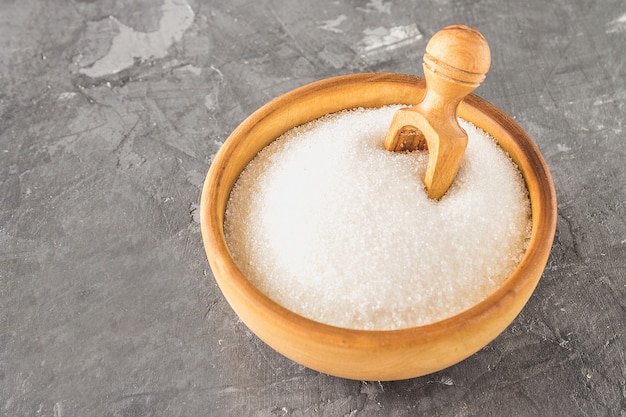 Açúcar de açúcar branco em uma placa de madeira com um dustpan em um fundo escuro.