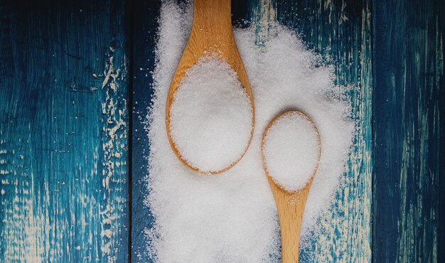 Foto açúcar refinado branco na colher deitado na mesa de madeira azul