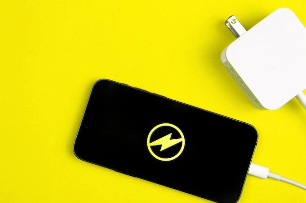 Adaptador de cargador de smartphone. Teléfono móvil con icono de energía en la pantalla. Fondo amarillo, foto vista superior