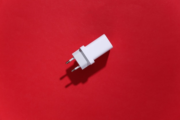 Adaptador de cargador sobre fondo rojo brillante con sombra profunda.