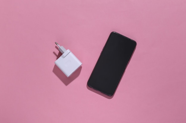 Adaptador de smartphone e carregador em fundo rosa brilhante com sombra profunda.