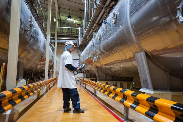 Adega de leite em pó do processo de inspeção do trabalho masculino na fábrica com tanques de aço inoxidável