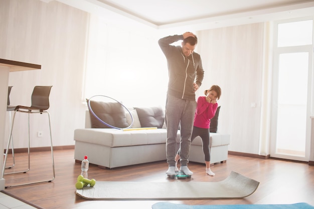 Adelgazar. Padre e hija se pesan en básculas domésticas de interior. Momentos divertidos y alegres divirtiéndose en familia. Dieta, nutrición adecuada y concepto de estilo de vida saludable.