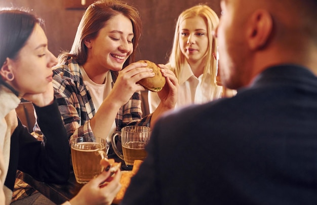 Adentro en el bar Grupo de jóvenes amigos sentados juntos con cerveza