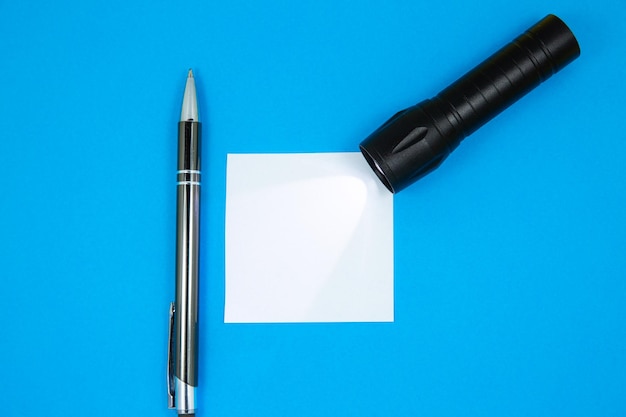 Adesivo de lista de tarefas em branco em branco com lanterna e caneta Pesquisando informações na Internet Close-up do papel de nota de lembrete no fundo azul Copiar espaço Minimalismo original e criativo