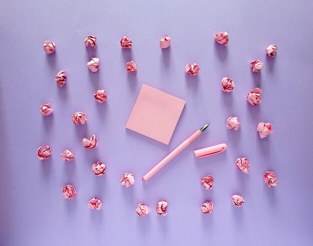 Adesivos de lembrete, caneta e bolas de papel amassadas em rosa sobre fundo roxo