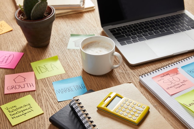Adesivos de papel com estratégia de negócios, xícara de café e laptop na mesa
