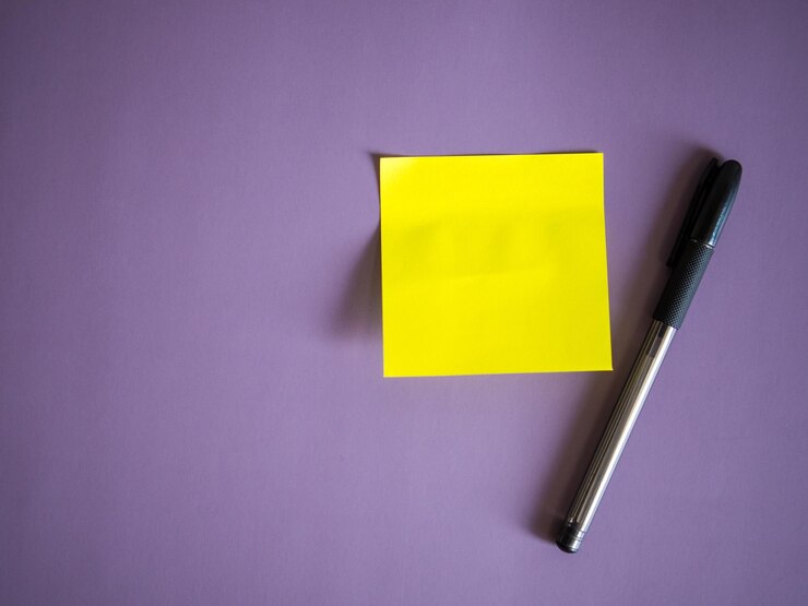 Foto adhesivo de papel amarillo en blanco para notas y bolígrafo sobre fondo morado