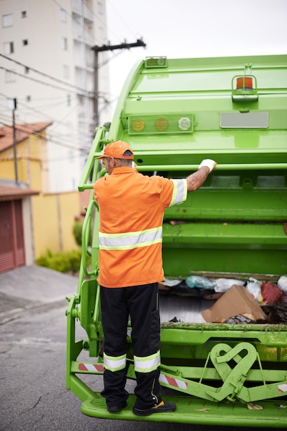 Foto adiante um trabalhador da coleta de lixo andando na traseira de um caminhão de lixo