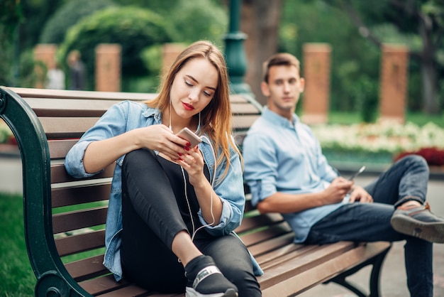 Adicción al teléfono, pareja sonriente en un banco en el parque