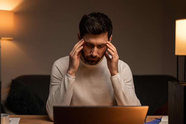 Adicción al trabajo, trabajando en una computadora portátil. Cansado empresario estresado con fatiga, depresión, problemas laborales, dolor de cabeza y migraña