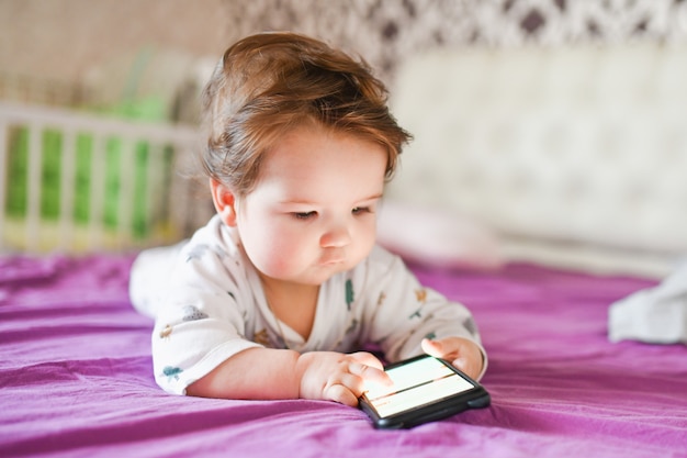 Adicción infantil a los teléfonos. radiación del teléfono al niño. Un niño de 0-1 años con un teléfono inteligente en sus manos mira la pantalla con entusiasmo. Adicción a los gadgets infantiles