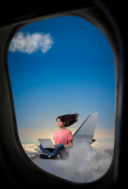 Adicción a la PC, mujer con portátil sentado en el ala del avión, vista desde el ojo de buey del avión