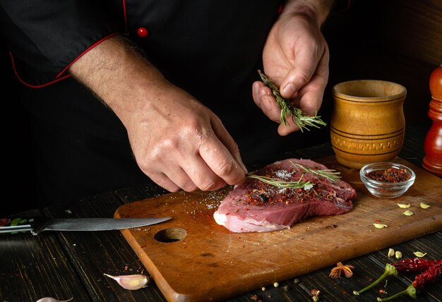 Foto adicionando alecrim ao bife para aroma e sabor cozinhar carne de vaca shish kebab na mesa da cozinha com as mãos de um chef