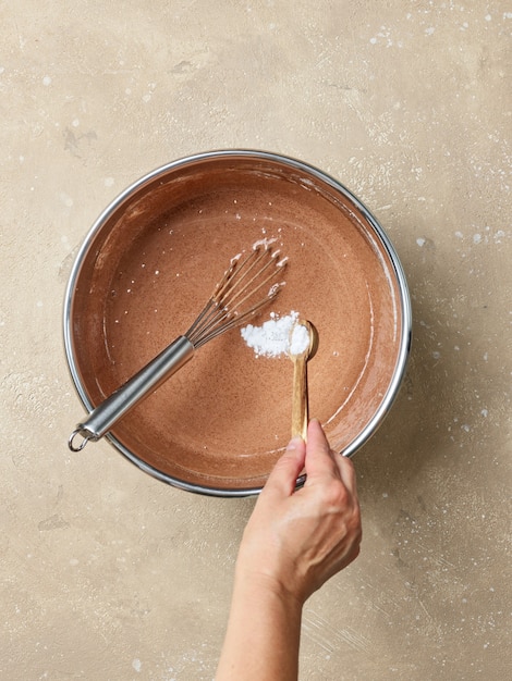 Adicionando bicarbonato de sódio em uma tigela de massa de bolo de chocolate, vista superior