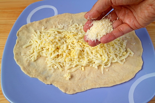 Adicionando queijo parmesão ralado à mão na massa coberta com queijo mussarela ralado