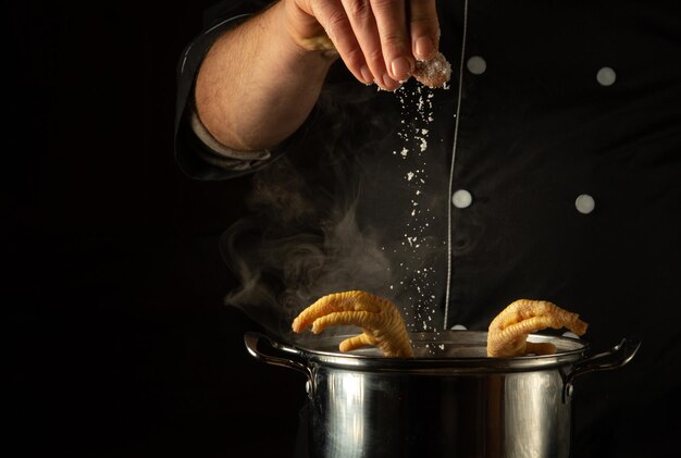 Adicionando sal com as mãos do chef a uma panela de pernas de frango fervendo Conceito de preparar um delicioso prato de acompanhamento em um restaurante ou cozinha de hotel