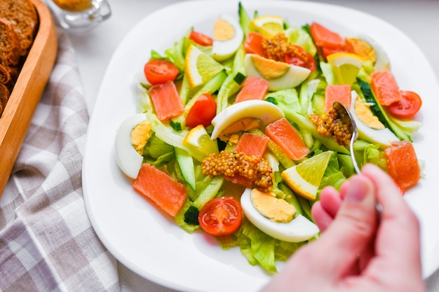 Adicione a mostarda à salada de legumes. salada de legumes com mãos humanas. num prato branco. adicione temperos.