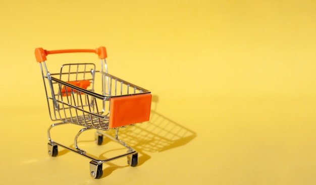 adicto a las compras Comprador. Concepto de compras. De cerca. Carrito de compras aislado sobre un fondo amarillo