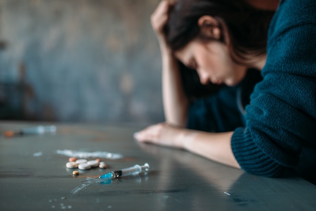 Foto adicto a las drogas sentado a la mesa con narcóticos