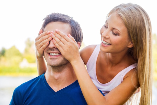 ¿Adivina quién? Hermosa joven cubriendo los ojos de su novio y sonriendo mientras ambos están de pie al aire libre