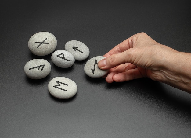 Adivinación con símbolos en piedra Mano sosteniendo piedras rúnicas nórdicas con símbolos negros